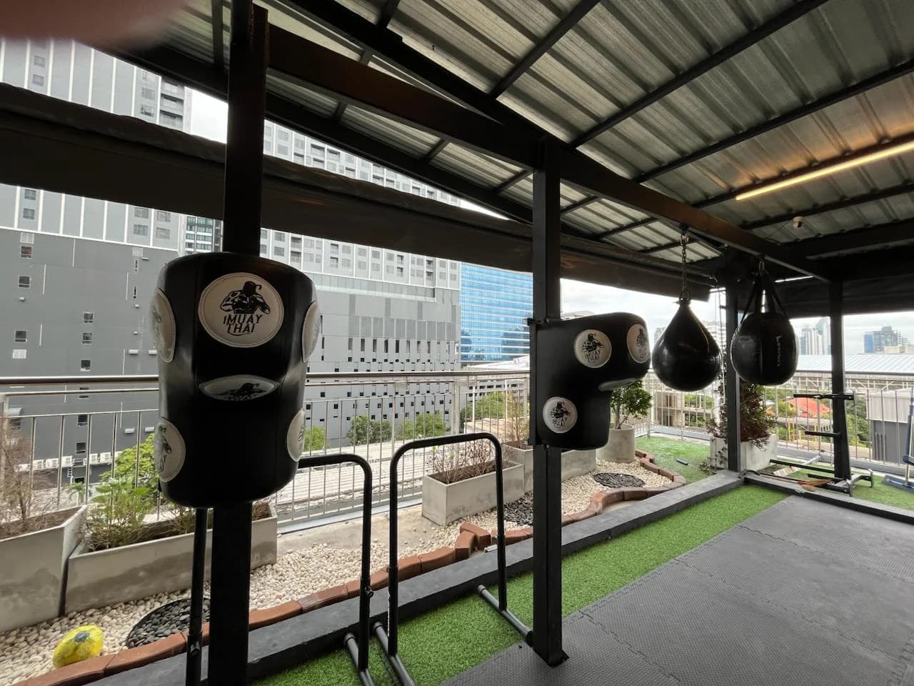 Open-air rooftop Muay Thai floor with heavy bags and Bangkok skyline at UnReal Gym